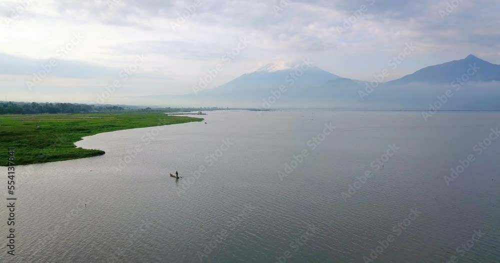 The fishing boat is on the huge lake looking for fish with mountain background - Rawa Pening Lake, Indonesia The fishing boat is on the huge lake looking for fish with mountain background - Rawa Pening Lake, Indonesia