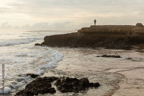 A lonely man stands on a rock by the ocean and looks at the waves