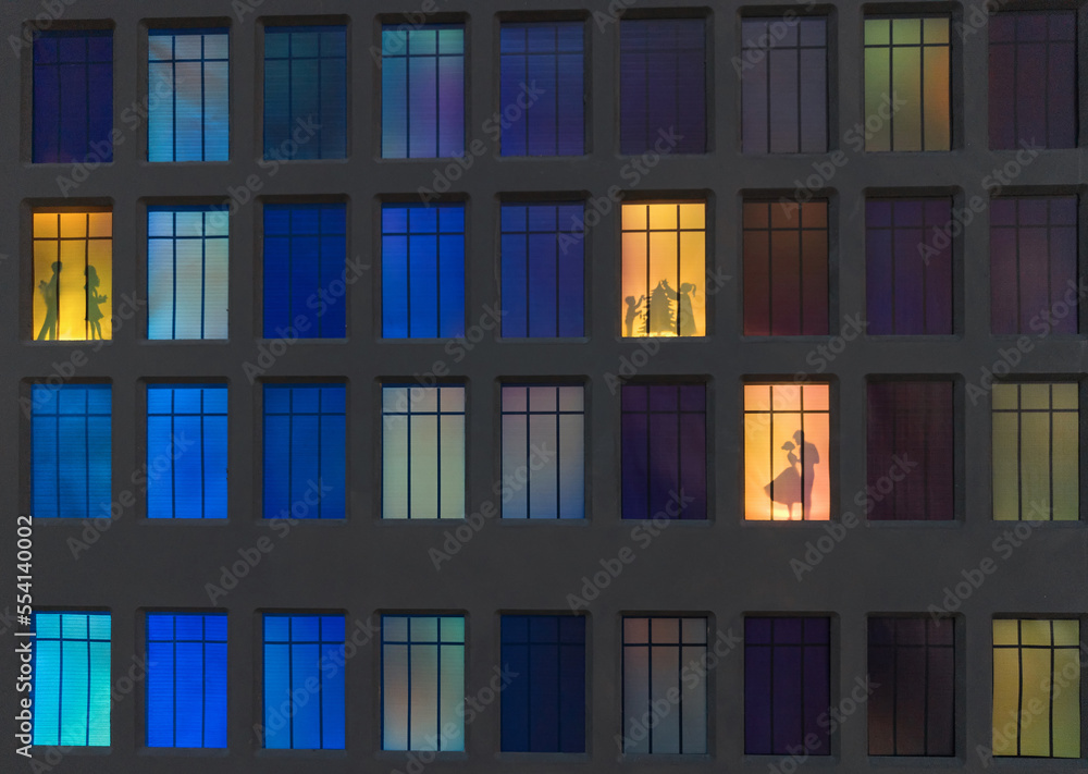 the wall of a night house in the illuminated windows of which silhouettes of people are visible the wall of a night house in the illuminated windows of which silhouettes of people are visible