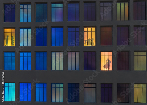 the wall of a night house in the illuminated windows of which silhouettes of people are visible