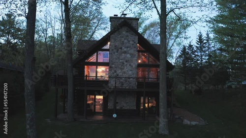 Aerial, exterior of wealthy expensive wooden cabin in the forest in the evening, lights on
