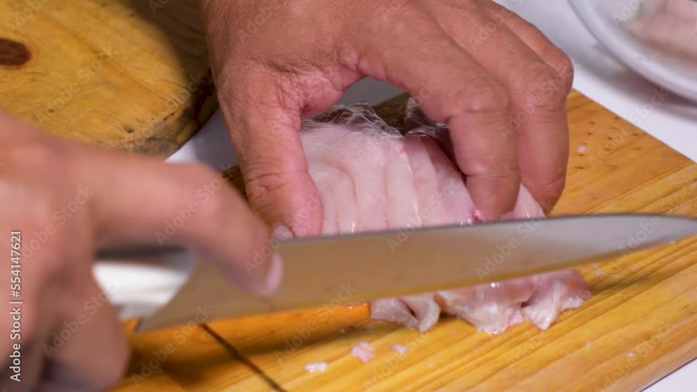 Hands of man cut raw chicken breast into squares on wooden cutting board Hands of man cut raw chicken breast into squares on wooden cutting board