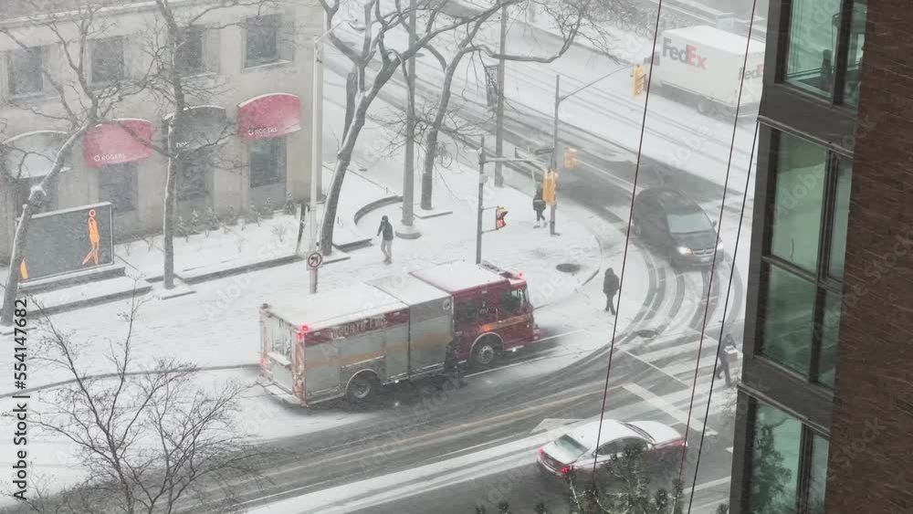 View Through Window Of Heavy Snow Falling On The Street With Vehicles And People Walking In Winter. Fire Engine Parked On Snowy Roadside. high angle View Through Window Of Heavy Snow Falling On The Street With Vehicles And People Walking In Winter. Fire Engine Parked On Snowy Roadside. high angle
