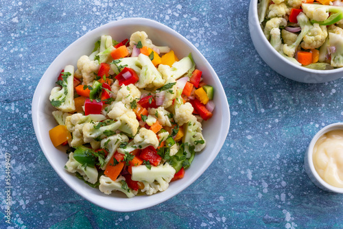 Healthy cauliflower salad in white bowl on blue wood background.
