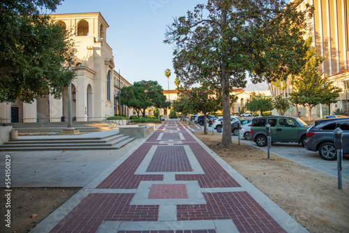 a long red brick sidewalk with parking meters and parked cars surrounded by buildings and lush green trees in Pasadena California USA photo