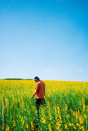 Portrait Asian man standing looking jute field. Yellow flower field at spring.