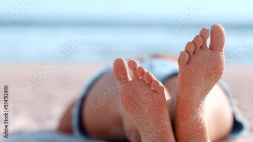 Feet, beach and summer with a woman lying on the sand by the sea or ocean while on holiday or vacation. Relax, legs crossed and foot sole with a female alone on the sunny coast during a getaway photo