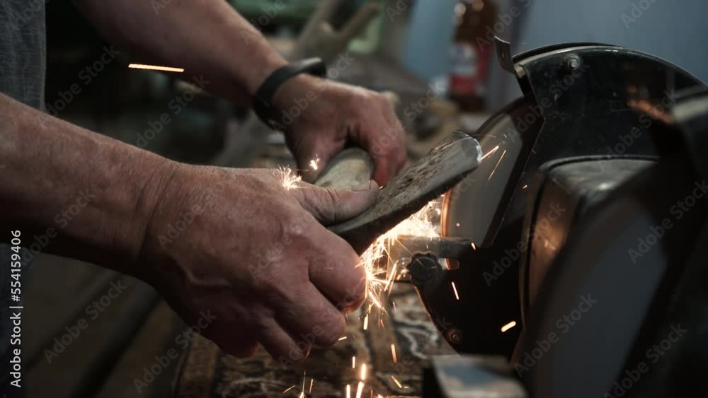 Sharpening an ax on an electric grinding wheel, Machine sharpening an ax on an electric grinder, hand sharpening on a rotating grinding stone, close-up. Sharpening an ax on an electric grinding wheel, Machine sharpening an ax on an electric grinder, hand sharpening on a rotating grinding stone, close-up.