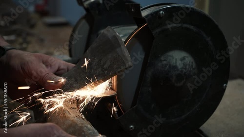 Sharpening an ax on an electric grinding wheel, Machine sharpening an ax on an electric grinder, hand sharpening on a rotating grinding stone, close-up.