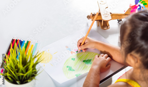 Asian cute kid preschooler sit on table smiling she draw picture with pencil at home  Happy child little girl colorful drawing family standing hold hands on planet earth on paper  earth day concept