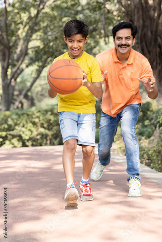 Father and son playing basketball at park.