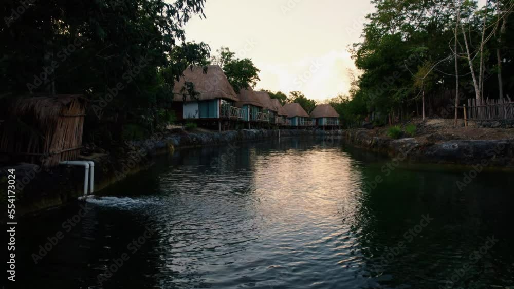 Aerial view over a river flowing through luxury beach wooden houses in a tropical resort surrounded by trees, in Tulum, Mexico, at sunset Aerial view over a river flowing through luxury beach wooden houses in a tropical resort surrounded by trees, in Tulum, Mexico, at sunset