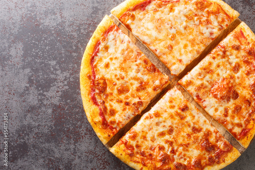 Delicious crispy New York style pizza with melted cheese and base tomato sauce close-up on a wooden board on the table. Horizontal top view from above photo