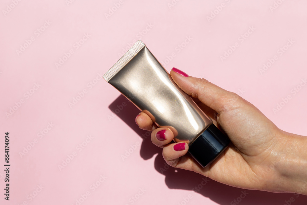 Close-up beautiful female hand with red nails holding cream tube on pink background with copy space. Manicure in trendy of 2023 year color viva magenta. Soft skin, skincare concept. Close-up beautiful female hand with red nails holding cream tube on pink background with copy space. Manicure in trendy of 2023 year color viva magenta. Soft skin, skincare concept.