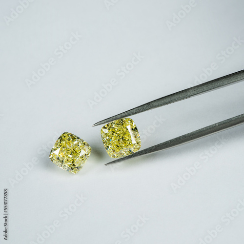 Cushion fancy yellow diamonds compare with tweezers on white surface