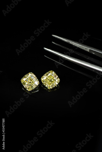 Cushion fancy yellow diamonds compare with tweezers on black reflection surface