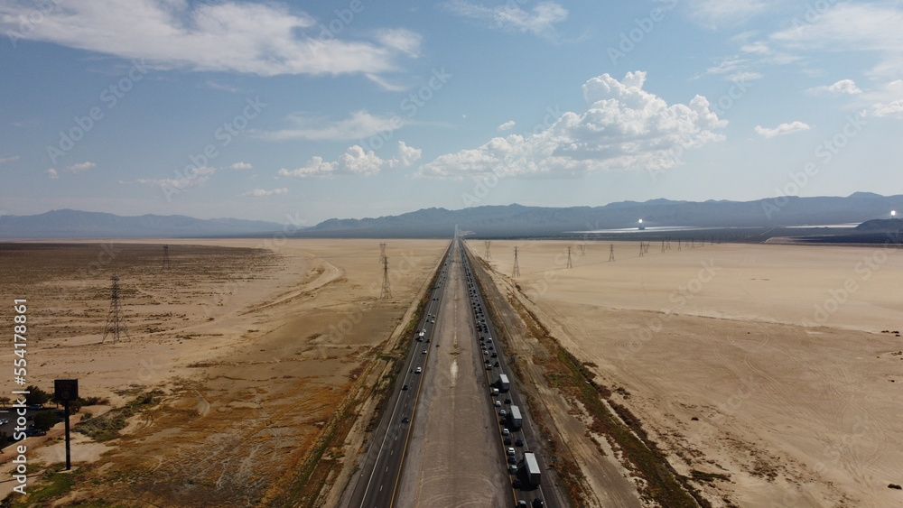 Fototapeta premium Aerial drone shot of state border between Nevada and California highway 15 facing South West during rush hour traffic on a clear sunny day with a cloudy sky overlooking Mojave National Preserve