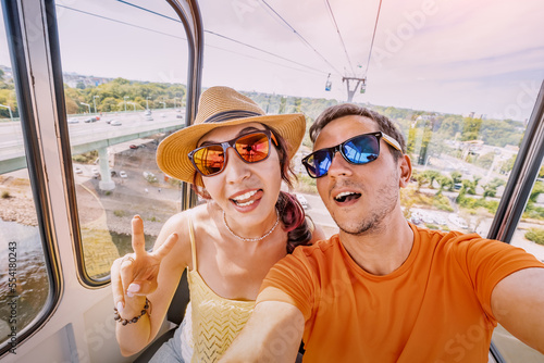 A couple of travel blogger girl and guy takes a selfie photo in a cable car with a view of the city of Cologne