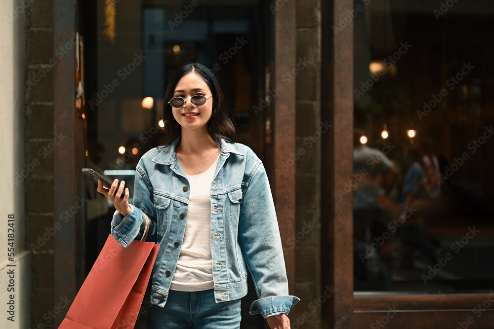 Obraz premium Asian woman holding shopping paper bags in hands walking outdoor at the shopping district of a city