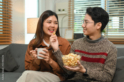 Young happy couple with popcorn watching tv at home. Leisure and people concept