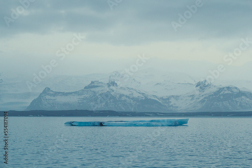 Flat iceberg floating in sea landscape photo. Beautiful nature scenery photography with mountains on background. Idyllic scene. High quality picture for wallpaper, travel blog, magazine, article