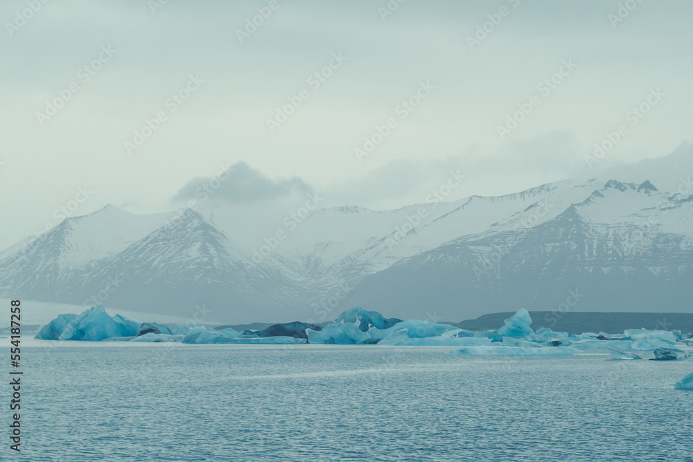 Icebergs in sea against mountains landscape photo. Beautiful nature scenery photography with grey sky on background. Idyllic scene. High quality picture for wallpaper, travel blog, magazine, article