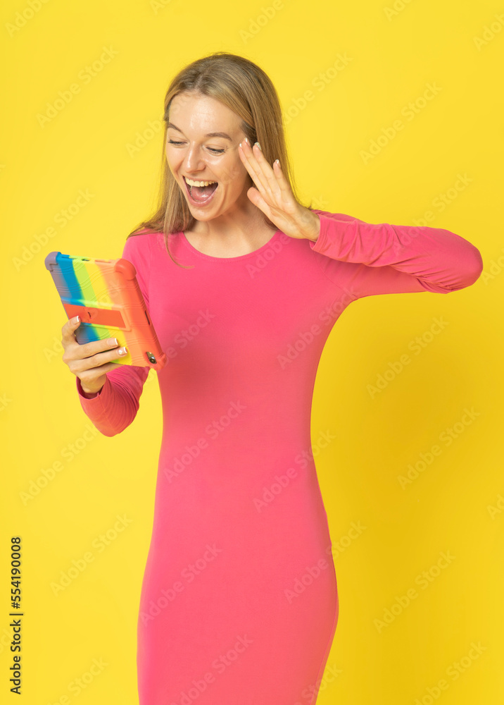 Attractive Young woman in red dress exciting using cellphone for selfie, videocall conversation, vlogging for social media and holding tablet pc, gesturing with hand isolated on yellow background. Attractive Young woman in red dress exciting using cellphone for selfie, videocall conversation, vlogging for social media and holding tablet pc, gesturing with hand isolated on yellow background.