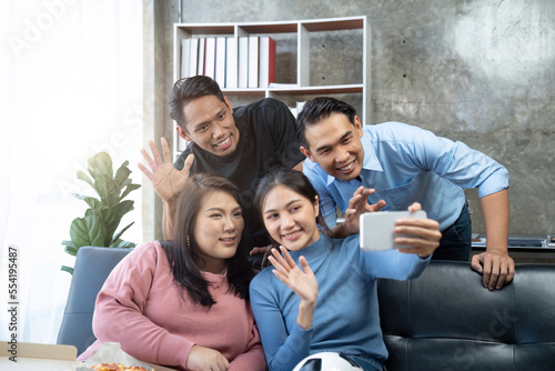 Friends watch sports on TV  cheer and celebrate. Happy diverse asian friend supporters fans sit on couch with popcorn and drinks. video call on mobile phone