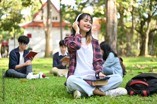 Charming Asian female enjoys listening to music through her headphones while sitting in the park.