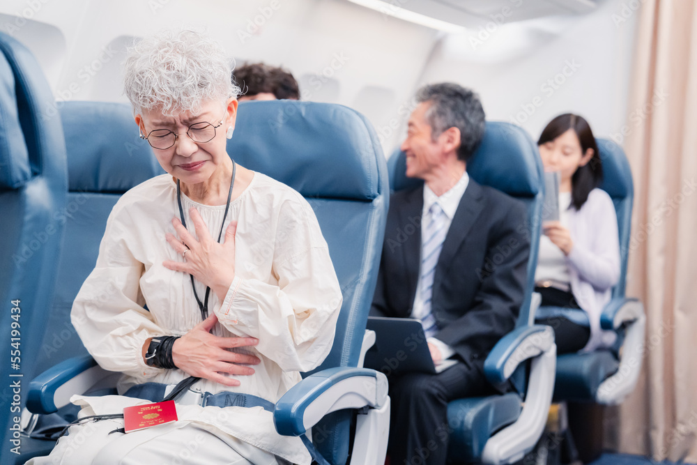 飛行機の機内で体調不良に苦しむ高齢の女性 飛行機の機内で体調不良に苦しむ高齢の女性