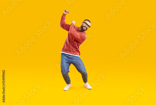 Cheerful, joyful and carefree man is having fun dancing on orange background in studio. Handsome and stylish Caucasian bearded man in casual clothes is dancing while waving his hands. Full length.