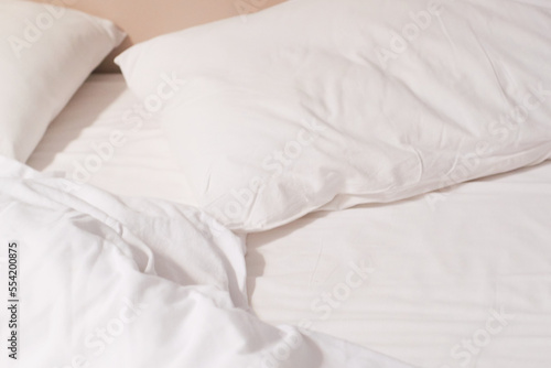 Wrinkled white blanket and pillows on comfortable bed in the morning.