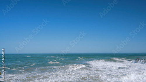 Storming sea . Action . Blue transparent water that is thrown out by waves to the shore against the background of a blue cloudless sky. © Media Whale Stock