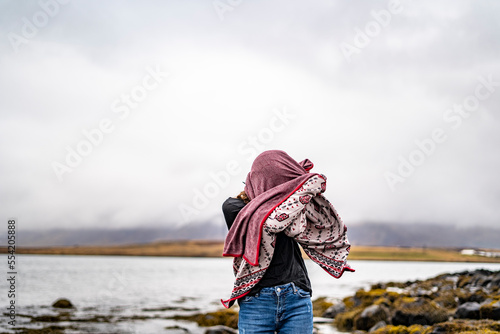 young woman covering her face with cardigan at rocky beach during winter