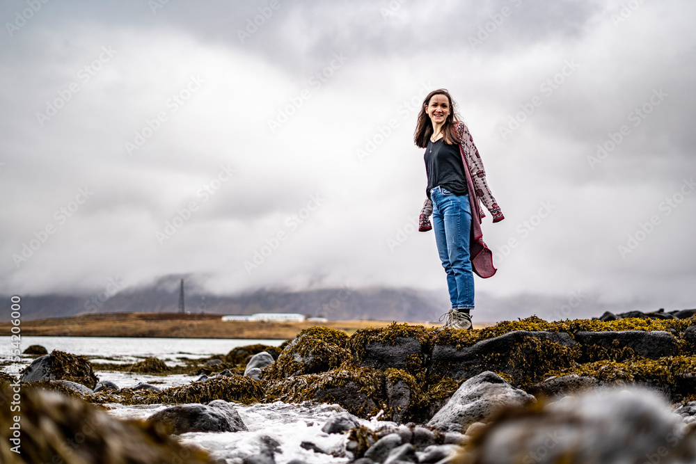Naklejka premium happy young woman in outerwear at rocky beach during winter