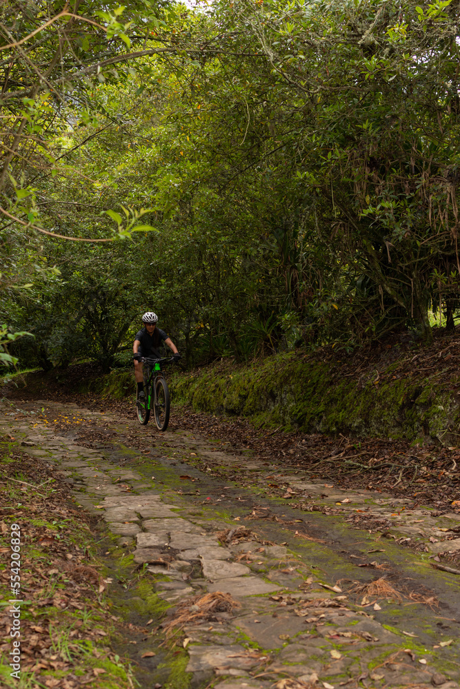 Unrecognizable cyclist woman, wearing glasses and helmet, riding her bike while descending a mountain on a stone path Unrecognizable cyclist woman, wearing glasses and helmet, riding her bike while descending a mountain on a stone path