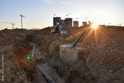 Sewer pipes laying. Sanitary drainage, external sewage. Tower crane on building construction. Excavator dig trench on construction site. Stormwater dig and pipe underground. Water infrastructure. photo