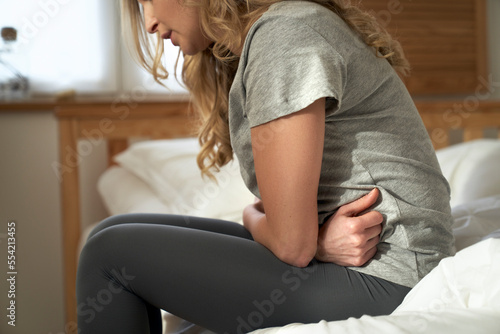 Close up of woman with pain of belly sitting on the bed at home