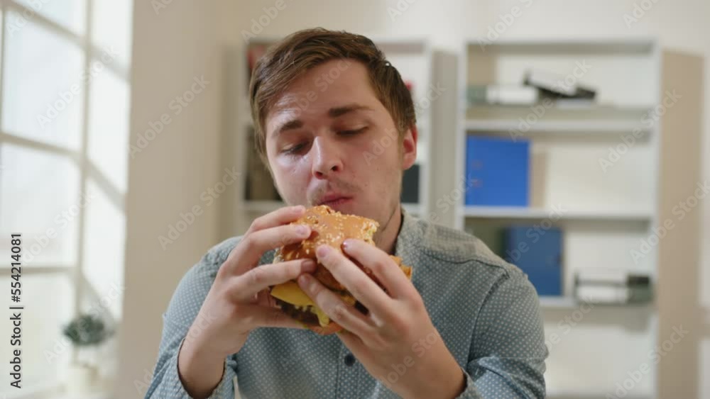 Portrait of man eating burger in office at lunchtime. Portrait of man eating burger in office at lunchtime.