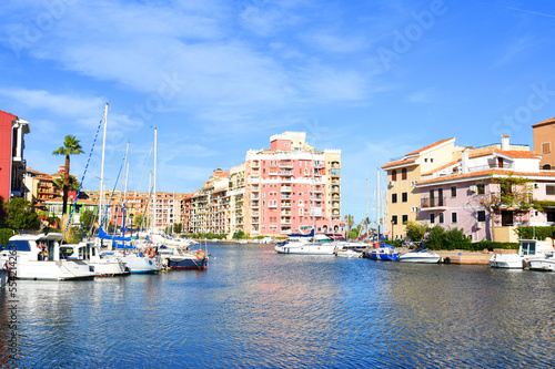 Jetty with yacht. Yachts and motor boats in marina Port Saplaya  Valencia. Yacht and fishing motorboat in yacht club. Colourful houses with apartments at coast Mediterranean Sea. Sailboat near pier.