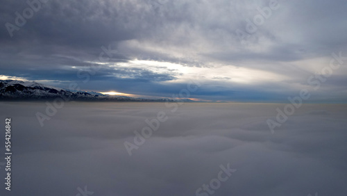 Flying a drone among the clouds with a view of the mountains. The light yellow rays of the sun at sunset are reflected on the surface of the clouds. Double layer of clouds. Mountains are visible © SergeyPanikhin