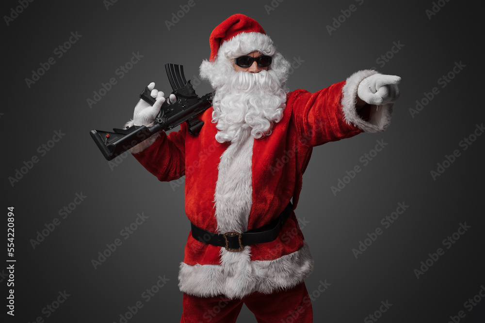 Shot of cool santa holding rifle on his shoulder pointing his finger away.