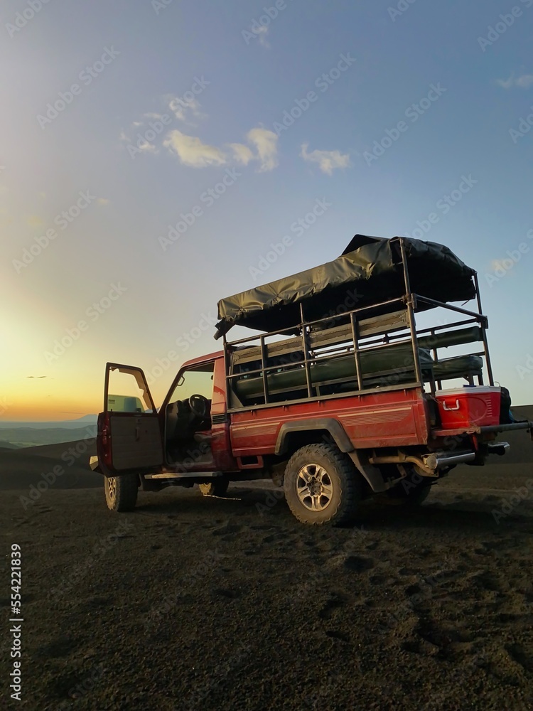 Pickup truck on dark black volcanic gravel during sunset. Pickup truck sunset scene. Sunset drinks. 'Cerro Negro' Nicaragua sunset scene. Volcano afternoon tour ending with drinks an the sun setting. 