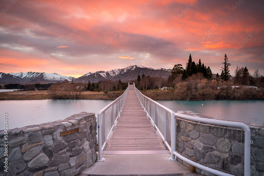 Sunrise view of the Maclaren Foot Bridge in late winter with beautiful snow capped Southern Alps mountain range in the background. Lake Tekapo, Canterbury, New Zealand South Island.