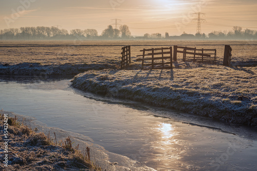 Dutch polder landscape on a cold day. The sun has just risen  it has frozen and there is ice on the ditch and frost on the grass. The photo was taken early in the morning in the Alblasserwaard region.