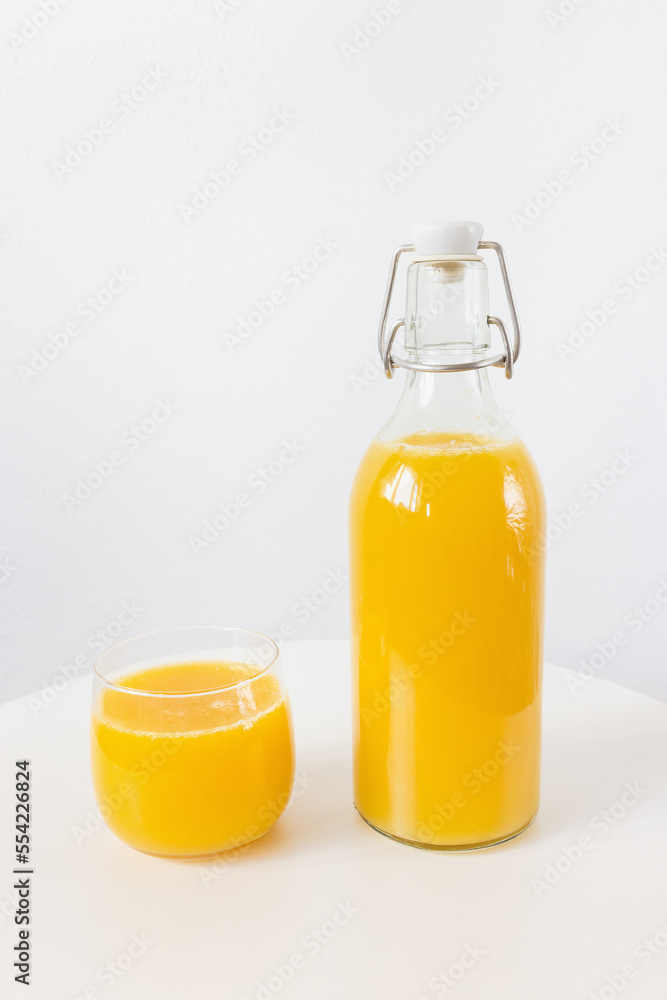 Fresh squeezed orange juice in bottle and glass on table on white Fresh squeezed orange juice in bottle and glass on table on white
