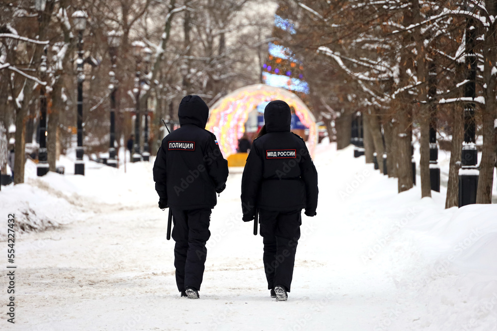 Russian police officers patrol a city street in Moscow on background of New Year decorations. Translation of inscriptions on the human backs: 