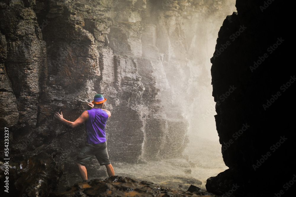 brave man entering powerful wide waterfall with white foaming water from a cave below