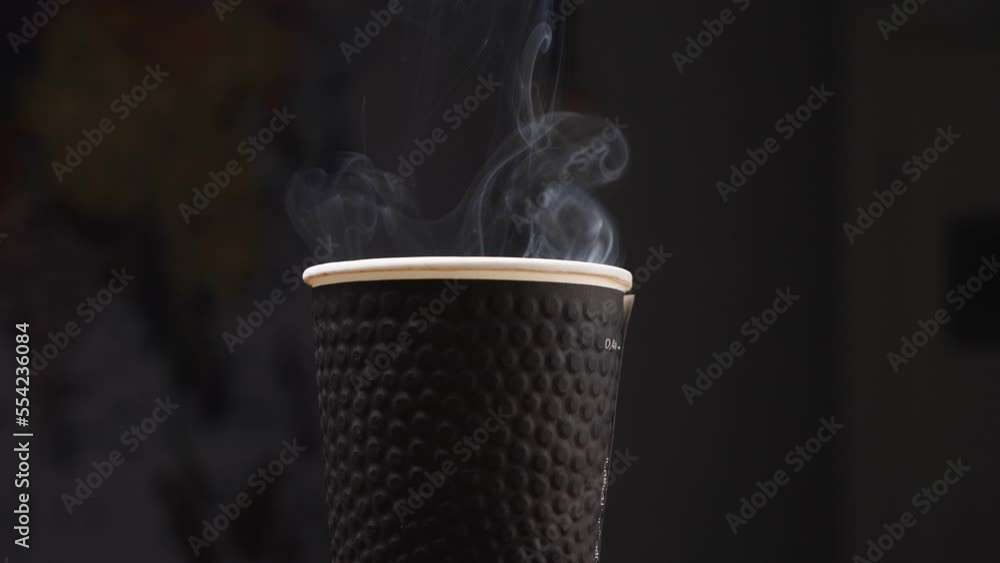 Close up of a black paper cup with coffee, from which the steam rises. Black background. Coffee shop concept. Fresh coffee every day. Slow motion Close up of a black paper cup with coffee, from which the steam rises. Black background. Coffee shop concept. Fresh coffee every day. Slow motion
