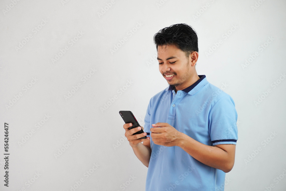 smiling or happy young handsome asian man holding phone wearing blue t shirt isolated on white background smiling or happy young handsome asian man holding phone wearing blue t shirt isolated on white background